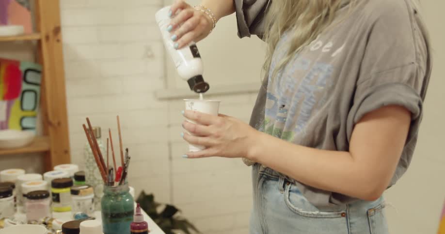 A woman pours a lotion from a bottle into a paper cup