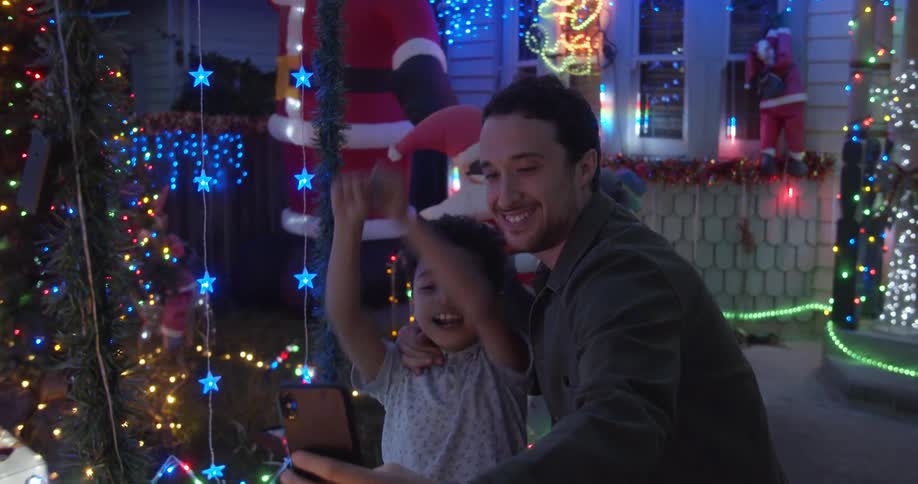 A father and son take a selfie together with outdoor christmas decorations and lights