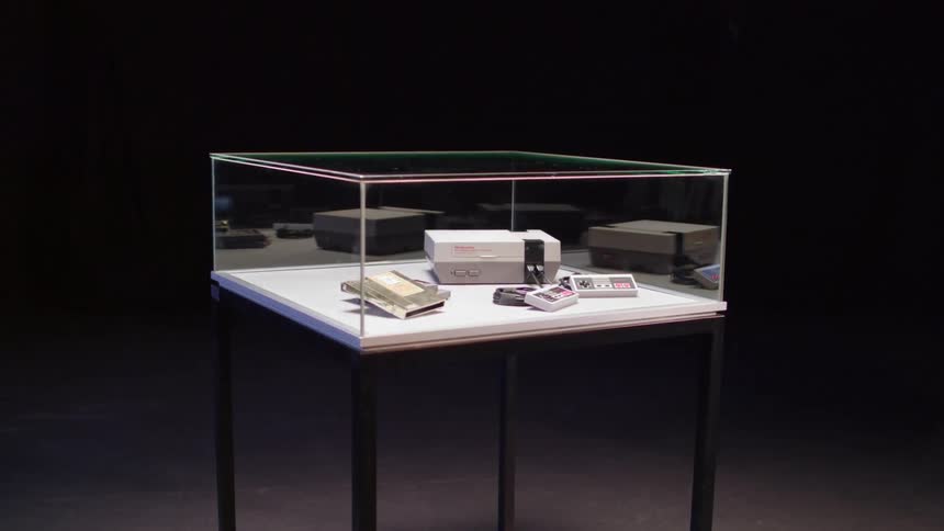 An original nintendo nes console controllers and games in a glass display shelf