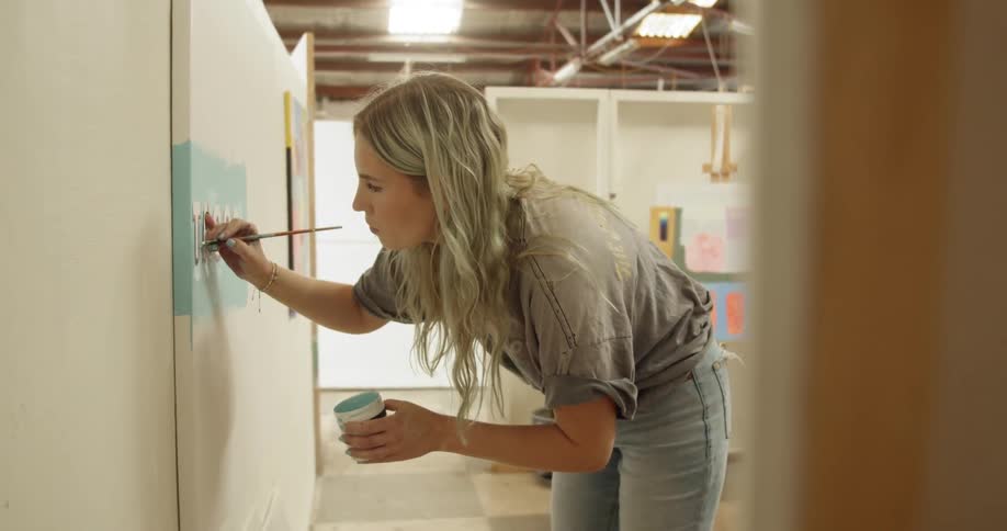 Blonde woman paints on a big canvas with a brush in the art studio