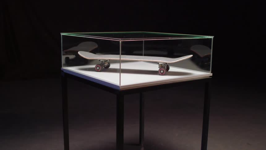A skateboard in a rotating display case in a dark room