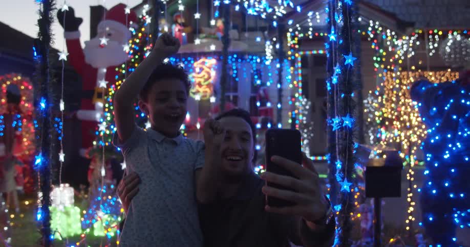A father and son take a selfie in front of a christmas light display