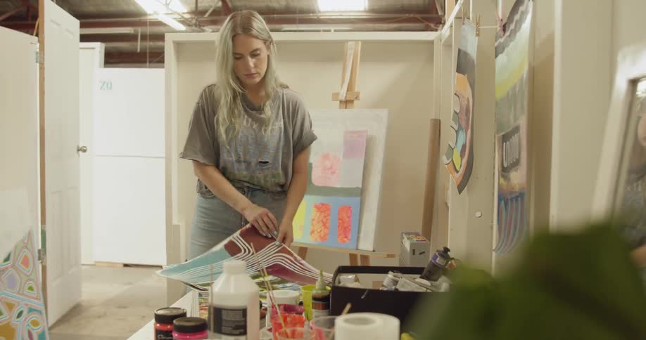 A woman goes through her paintings on a table