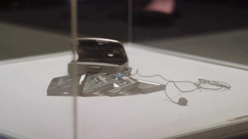 A cassette player and cassette tapes are on display in a glass case