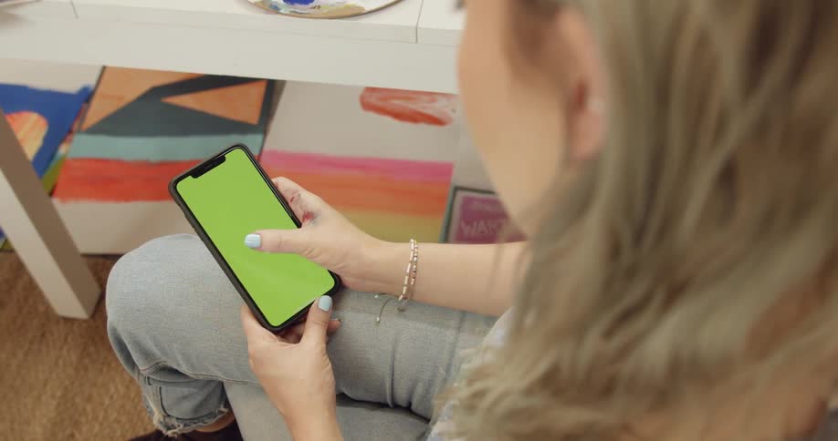 A woman swipes across her smartphone while seated beside a table