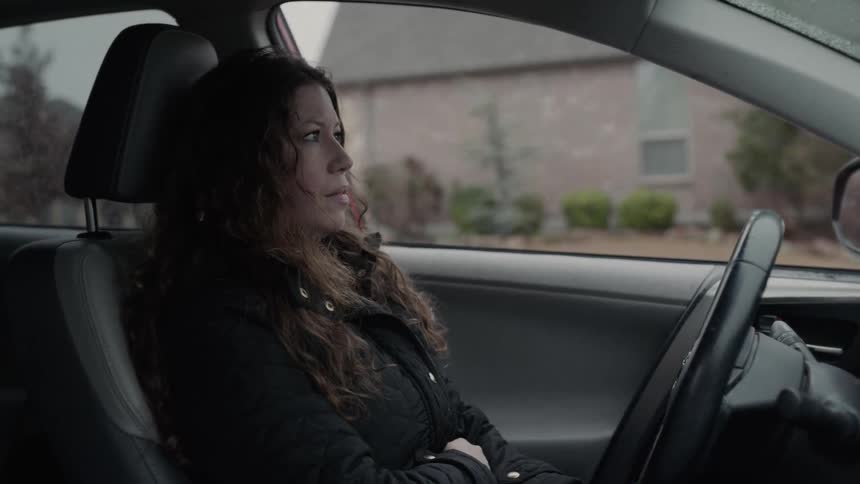 A woman who looks upset sits in the drivers seat of a vehicle