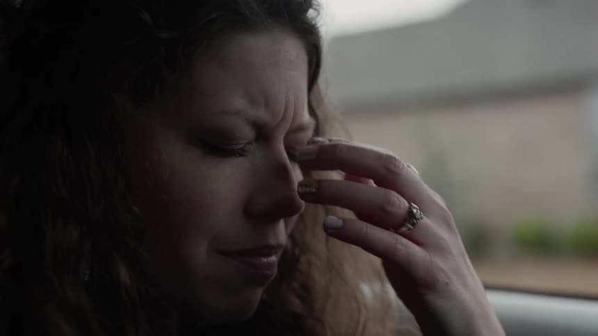 A woman sits in her car while she is clearly thinking about something that is upsetting her