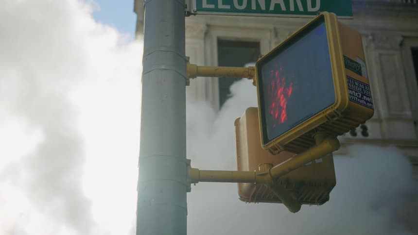 A crosswalk sign with a building and steam in the background