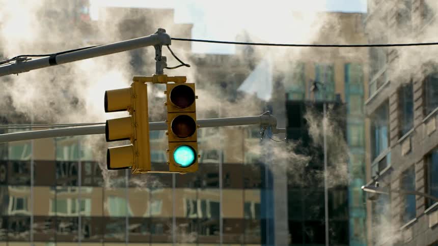 Smoke flows past green lit traffic light next to building