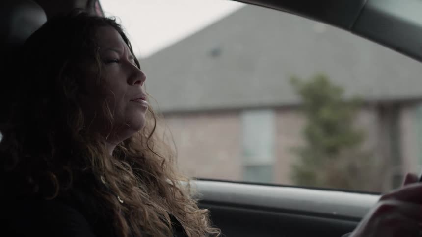 A woman sitting in a car is clearly upset and places her had on her face while breathing deeply