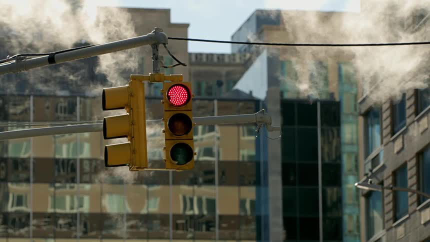 Steam wafts past a city traffic light that is illuminated red