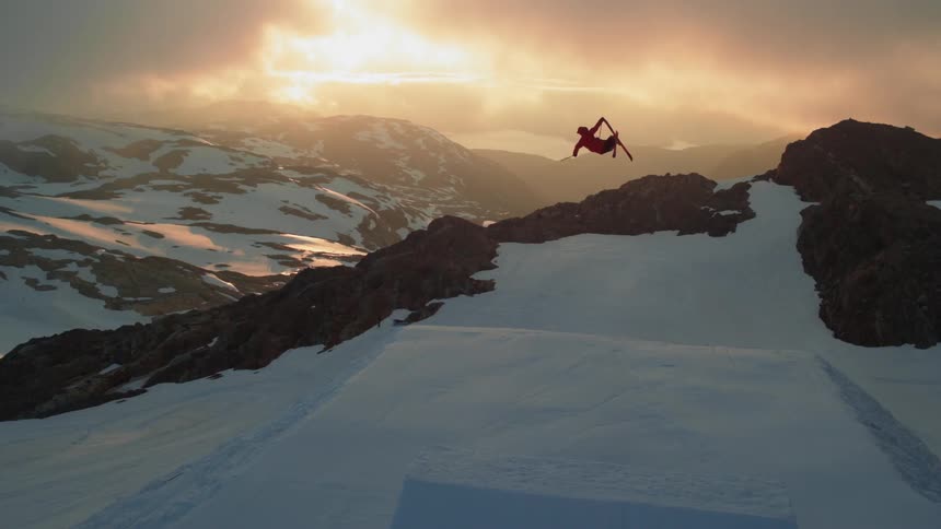Aerial view of skier jumping from ramp on snowy mountain at sunset
