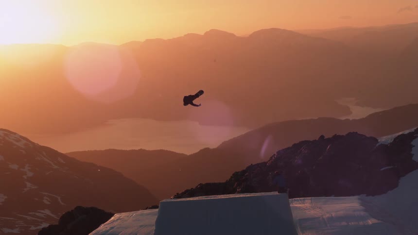 A snowboarder jumping a snow ramp outside near mountains