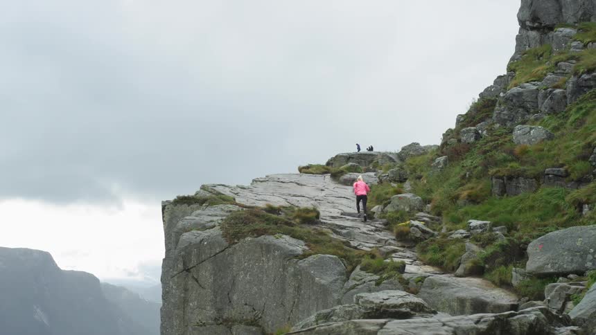 Woman jogs up stone mountain slope near cliff edge