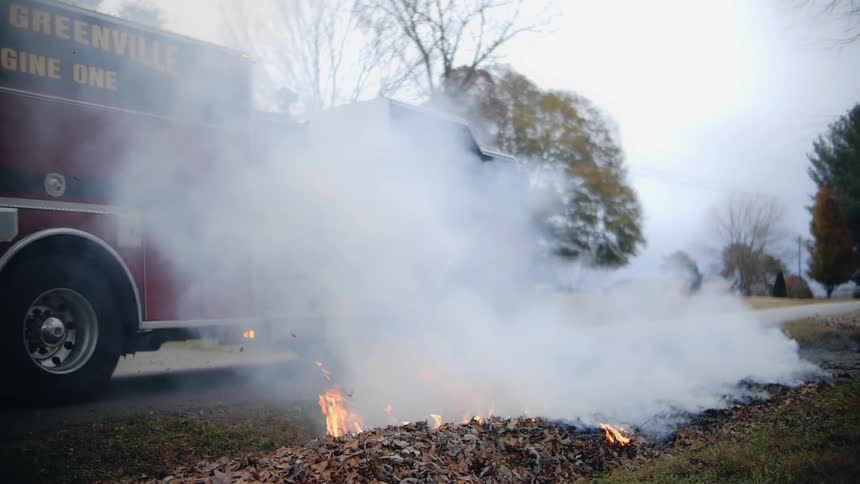 A firetruck drives down a road next to a burning pile of leaves