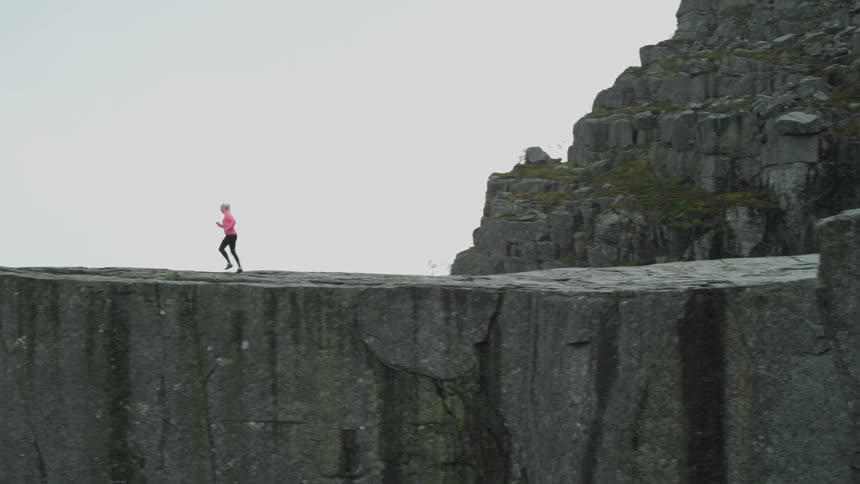 Blonde woman runs up to the cliffside on a cloudy day