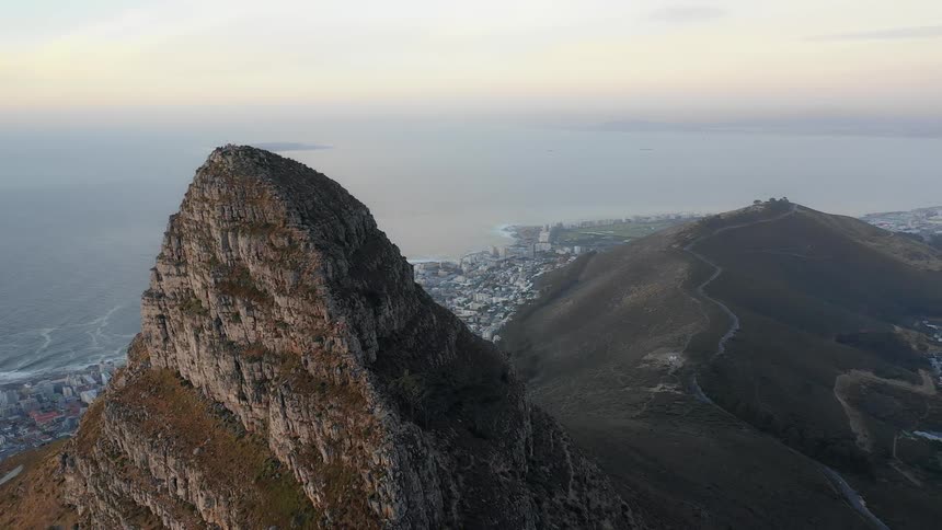 A large rock formation towers high above a dense coastal city