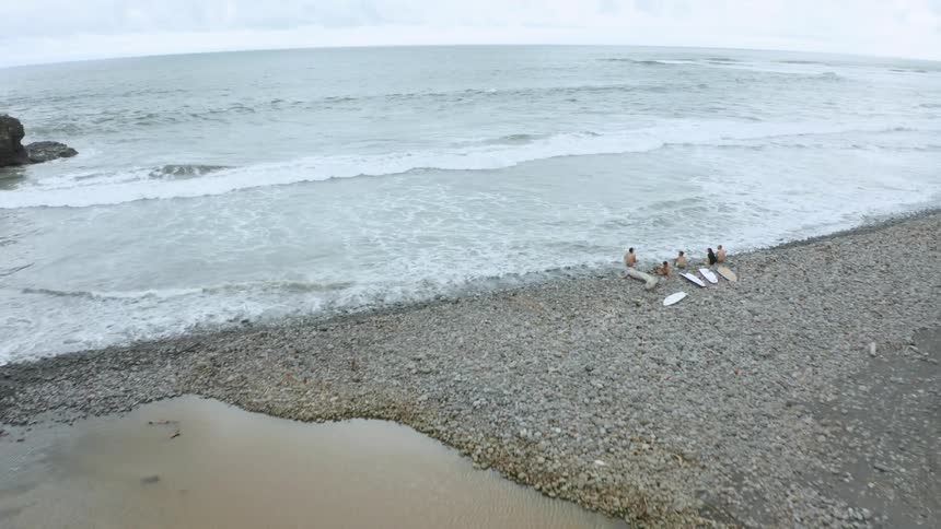 People are sitting on the shore with their surfboards