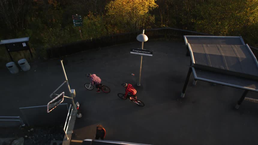 Two people ride bicycles beside a train and head towards a woody area