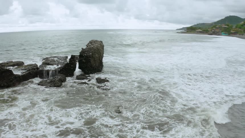 Surf crashes past cluster of bouldersonto beachnear huts
