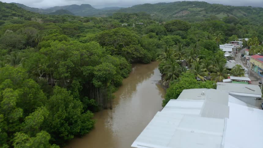 A shack city on a muddy river near trees and mountains