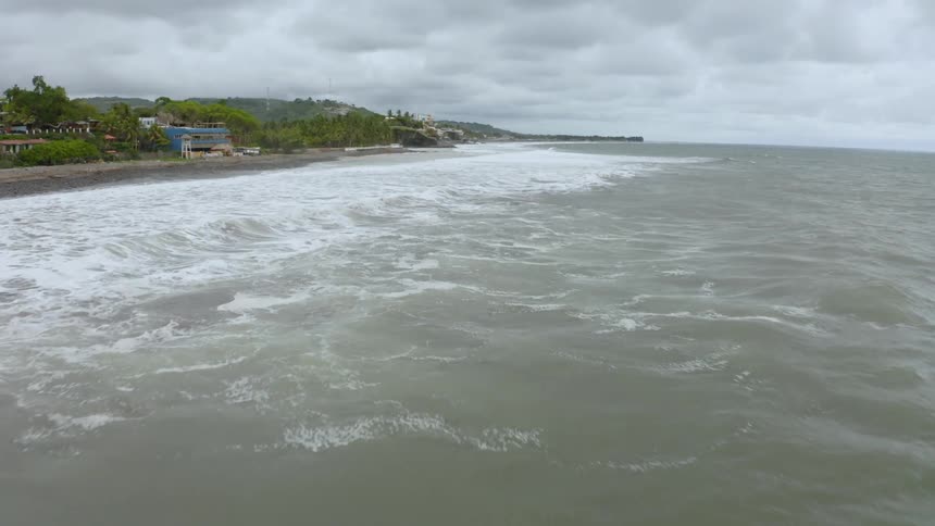 An aerial view of the ocean moving towards the beach is displayed