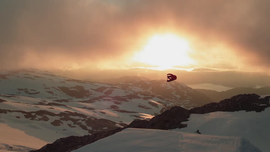 A skier does a trick off of a ski jump during sunset on a mountain