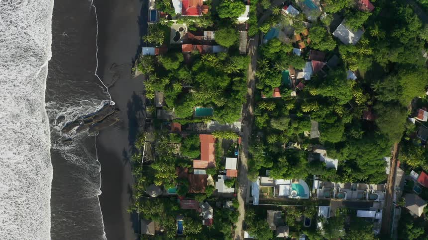 A residential neighborhood sits adjacent to a beach covered in dark sand