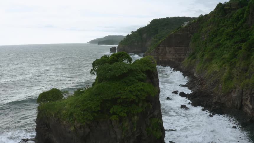 A rocky coastline with a tree topped island amidst the crashing waves