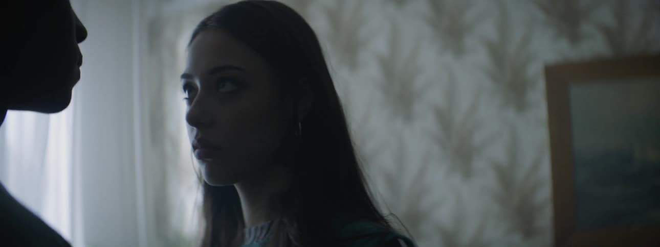 A woman stares at a man standing in front of her with a frightened look on her face