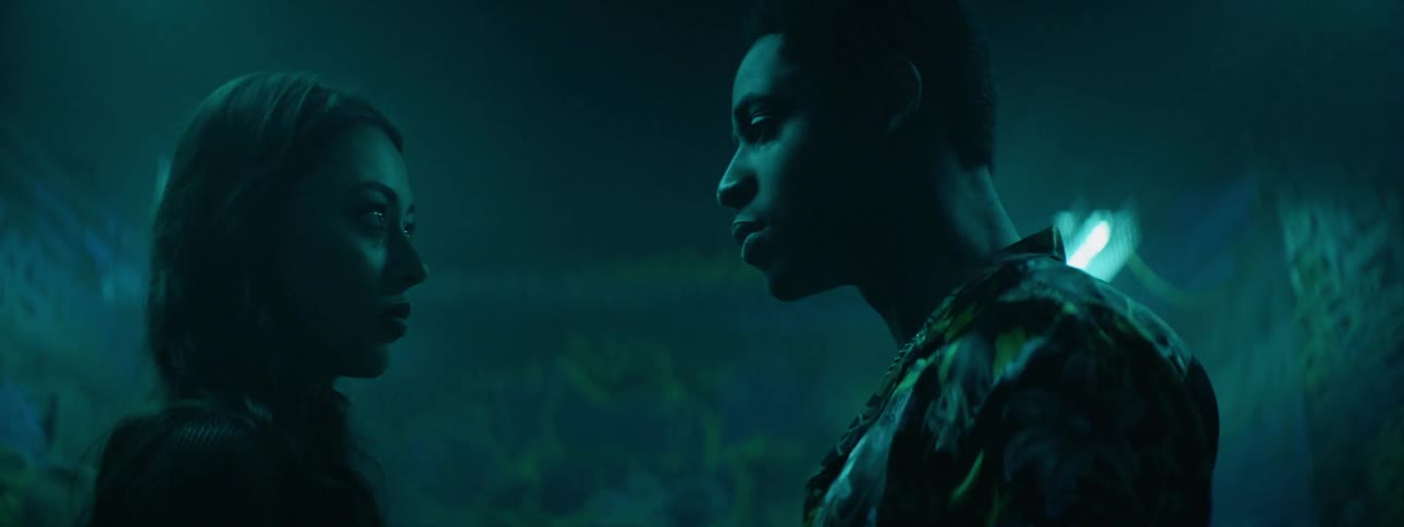 A young man and woman stare intensely at each other within a club with bright flashing lights