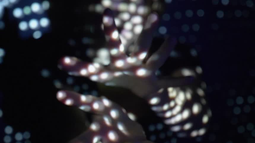 A woman moves her hands as lights shine and reflect on her
