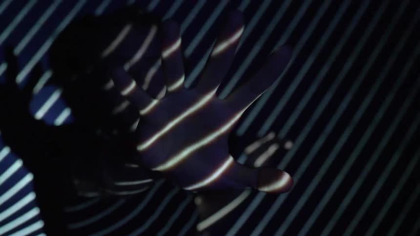 A woman in the dark reaches out as lights flash over her