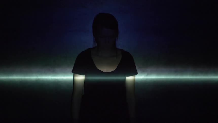 A woman is standing in the dark and several lights flash over her