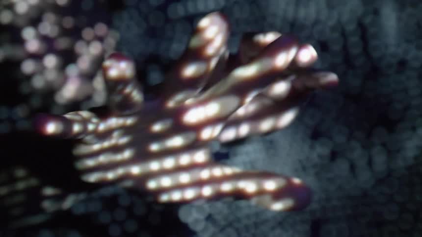 A person standing in a dark room holds out their hands as different patterns of lights are projected upon them