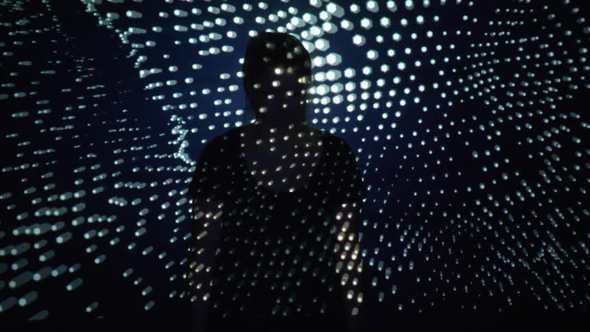Abstract light patterns are being projected onto a person in a dark room