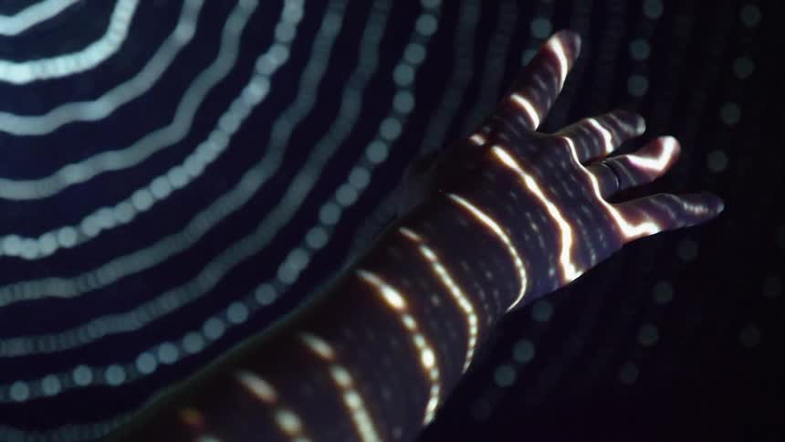 A woman holds her hand in front of lights so it makes a design on her arm