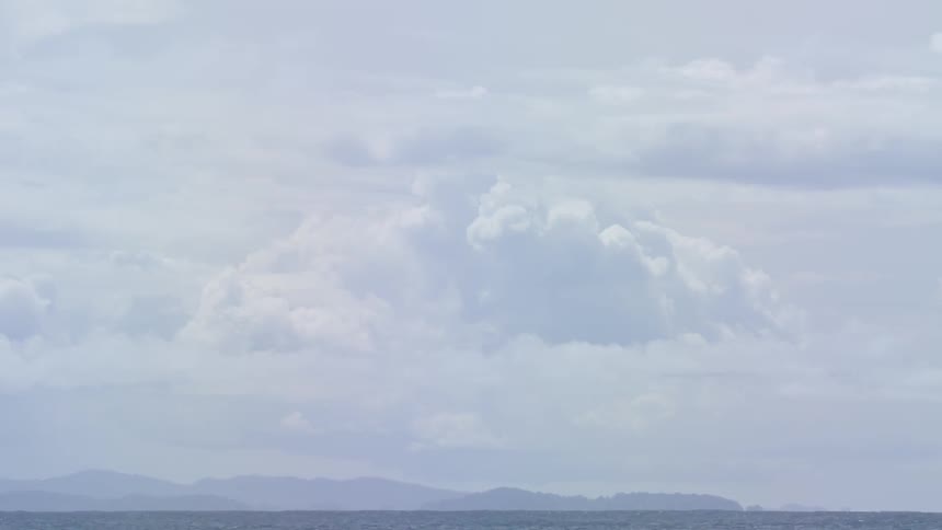 Clouds swirl above the ocean with an island in the distance