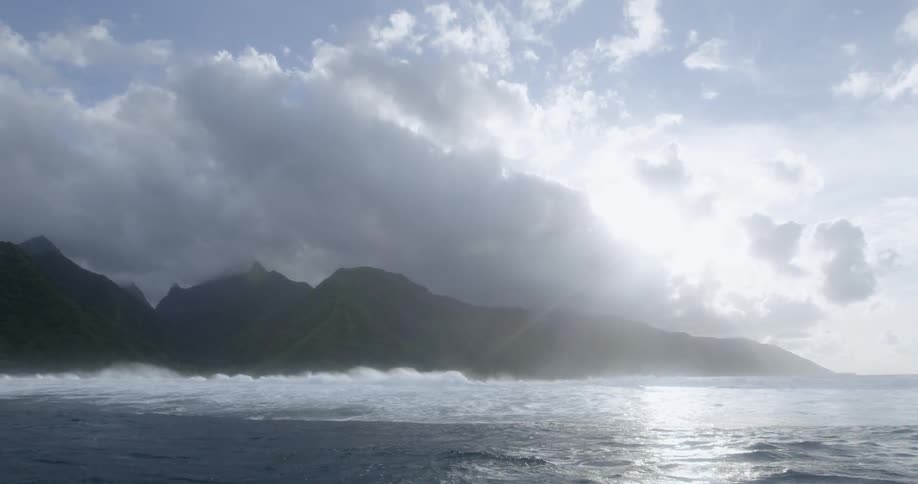 The sun shines through the clouds to illuminate an island in the ocean