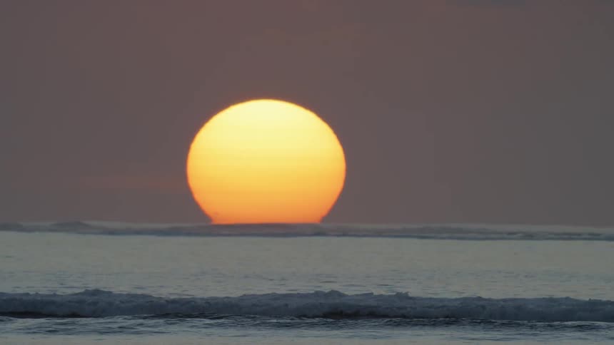 The sun is setting behind the ocean