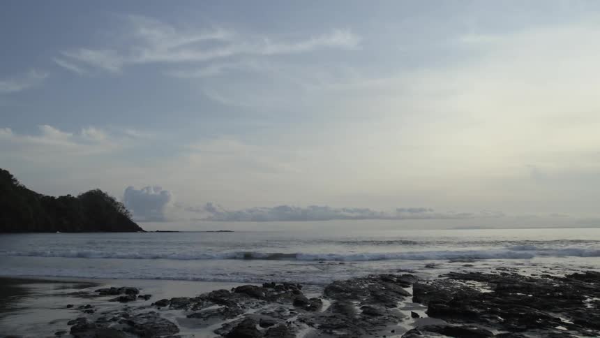 Waves roll onto the beach near rocks on cloudy day