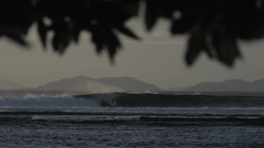 Large wave breaks with mountains on the horizon