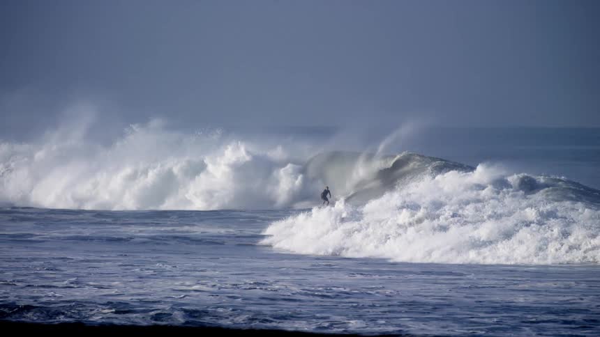 A surfer rides an enormous ocean wave