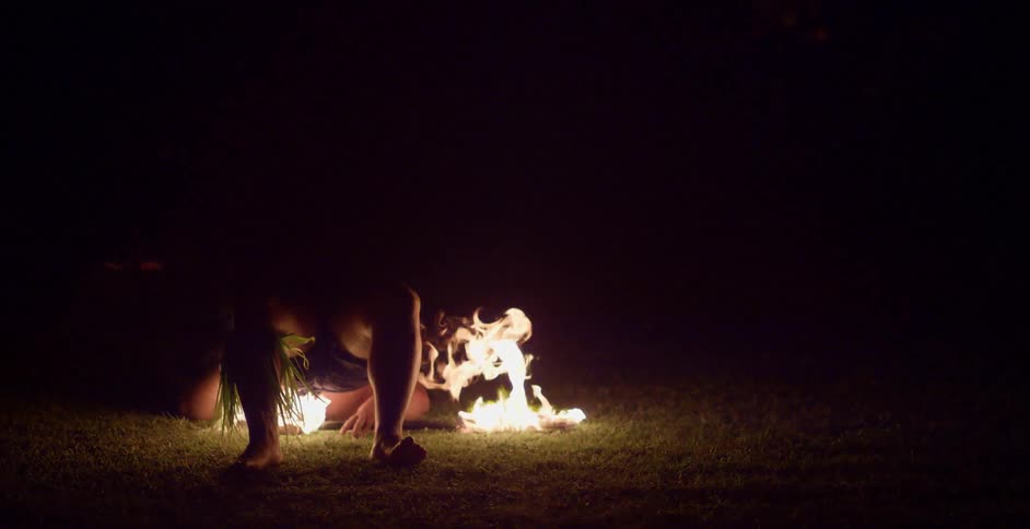 Man performs with flaming button on field in the dark