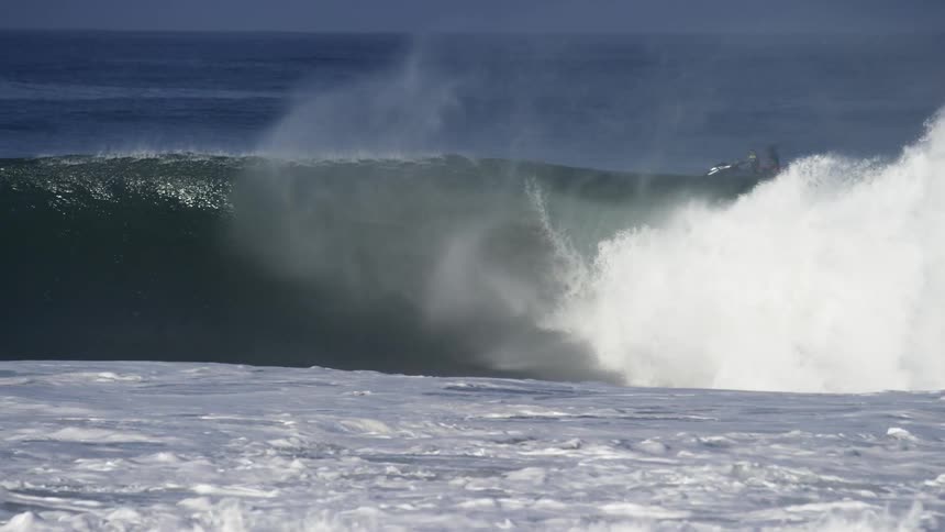 An ocean wave rolls and curls to form a tube on a sunny day