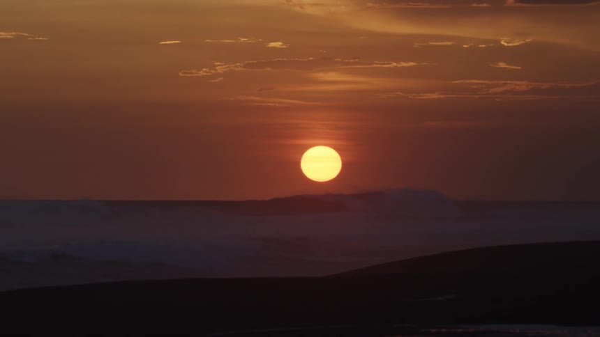 Landscape view of the sun setting as waves wash towards the shore