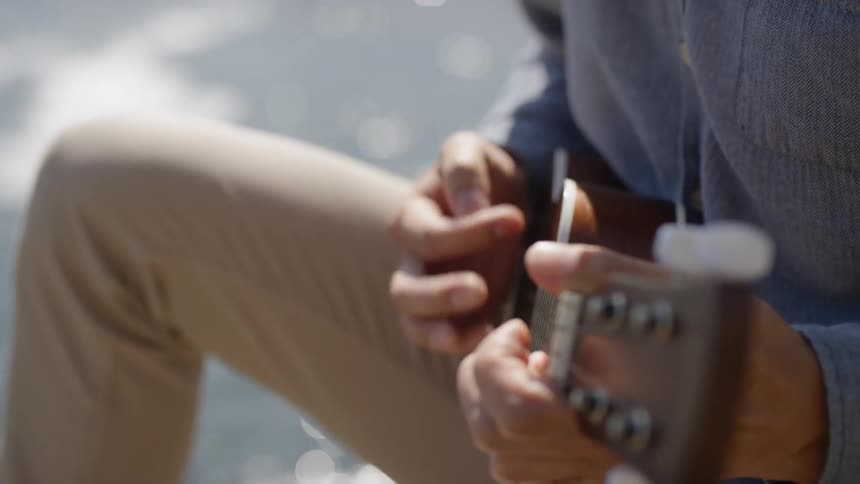 Man plays on ukulele with ocean and beach in the background