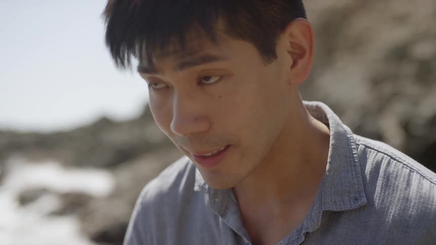 Close up of an asian man smiling and relaxing by the shoreline