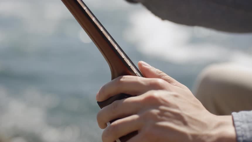 A man is holding an instrument by the ocean