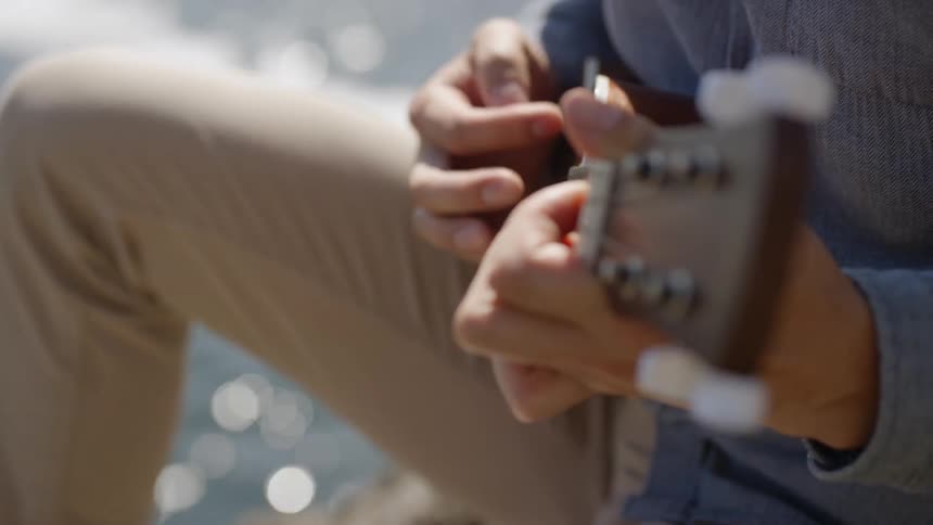 Asian man playing a ukulele by the shoreline